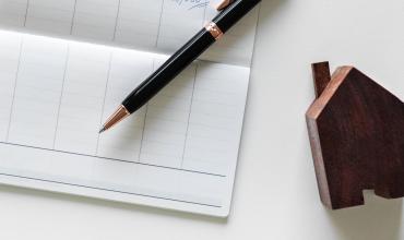 $7M Grant Will Provide Rent Assistance for North Carolinians with Disabilities a checkbook, pen and wooden toy house on a table