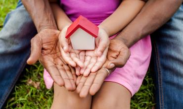 A dad and his daughter holding a mini house on their lawn