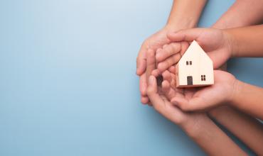 Hands holding a little house against a blue background