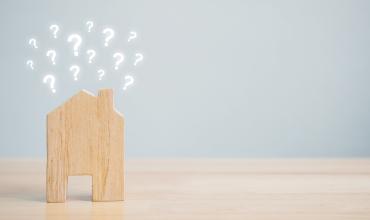 Small wooden house sitting on a desk with little question marks coming out of the roof