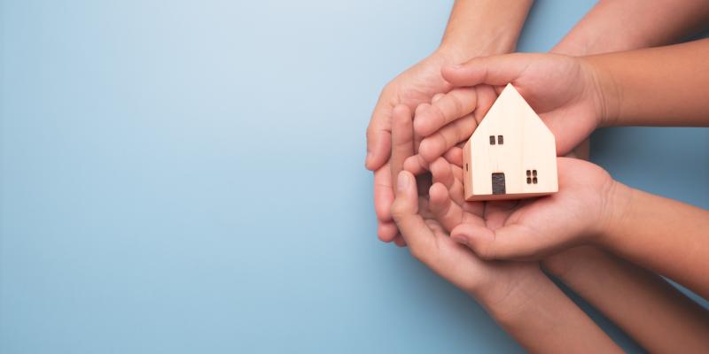 Hands holding a little house against a blue background