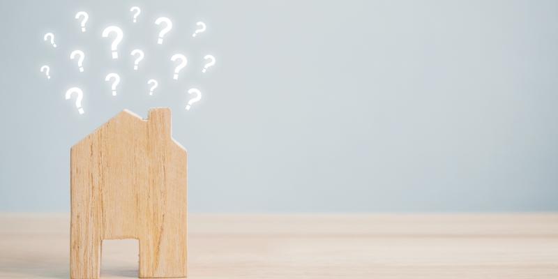 Small wooden house sitting on a desk with little question marks coming out of the roof